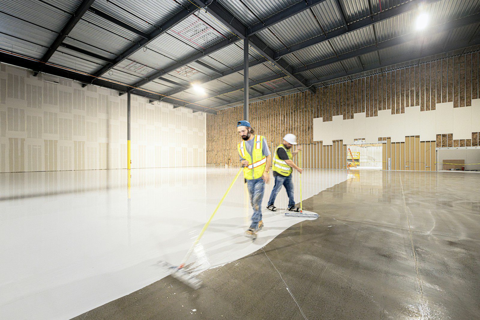 Workers painting the floor of a large empty warehouse.